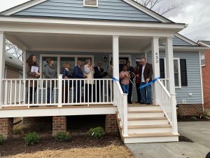 Ms. Harris and two of her children celebrate their accomplishment on the front porch of their new blue, single-story home.