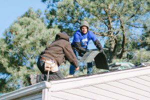 Two men remove and replace shingles on a one-story home.